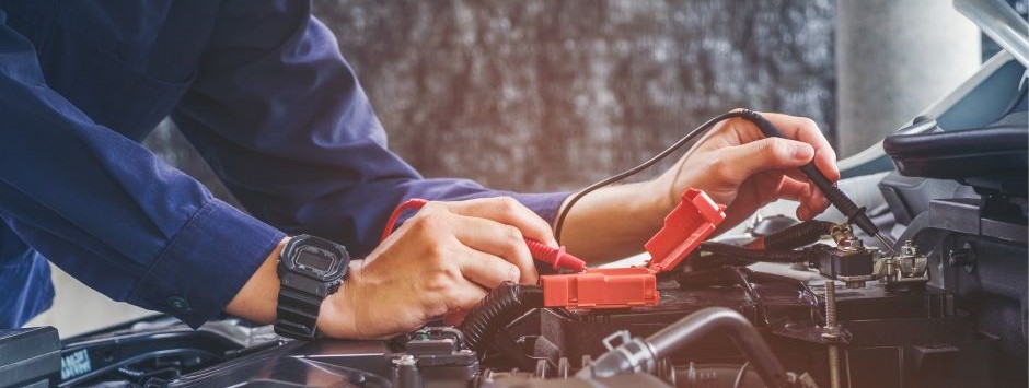 Mechanic testing car battery under the hood of a vehicle